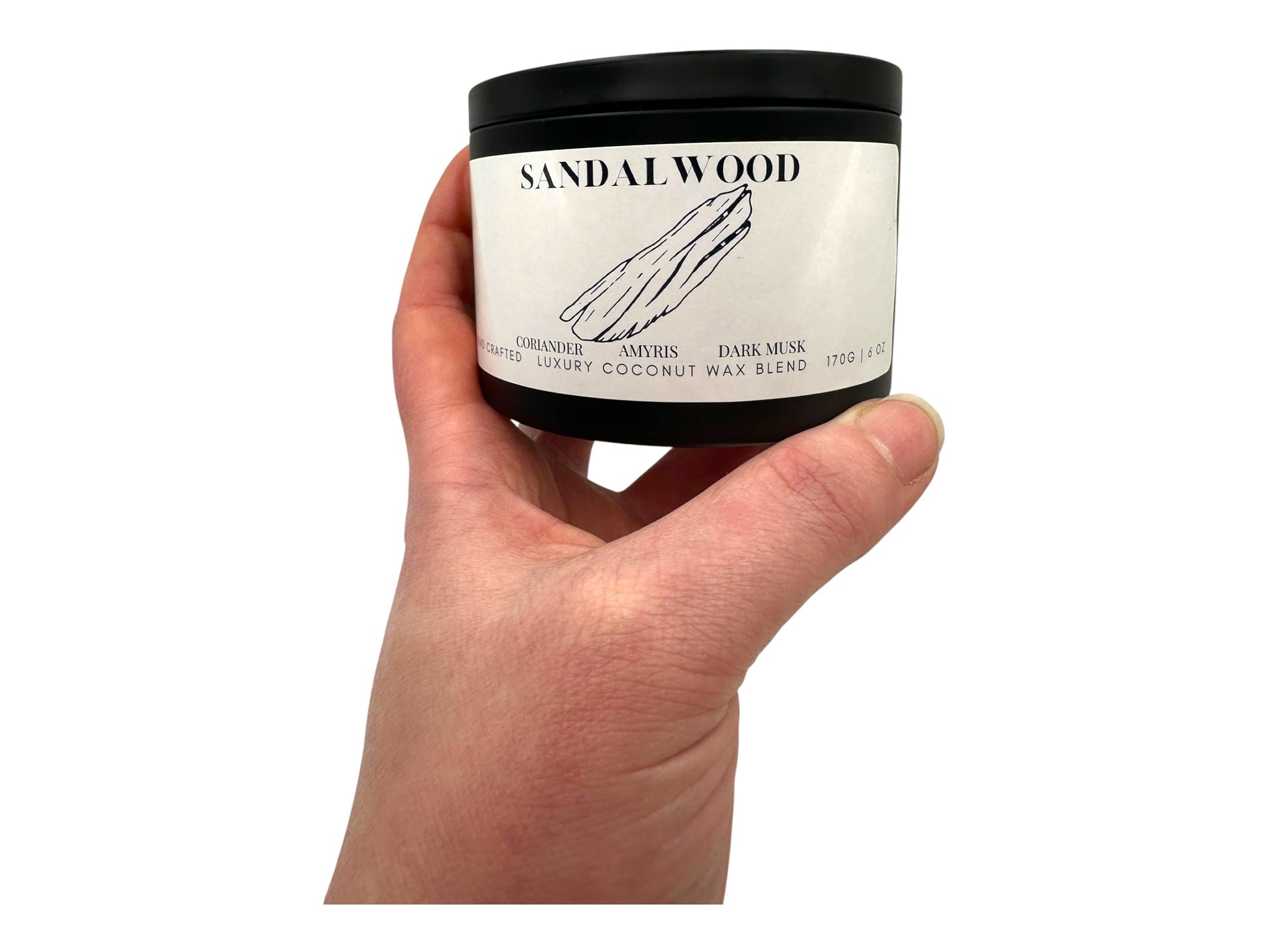 A hand holding a black candle tin labeled "Sandalwood" on a white background.