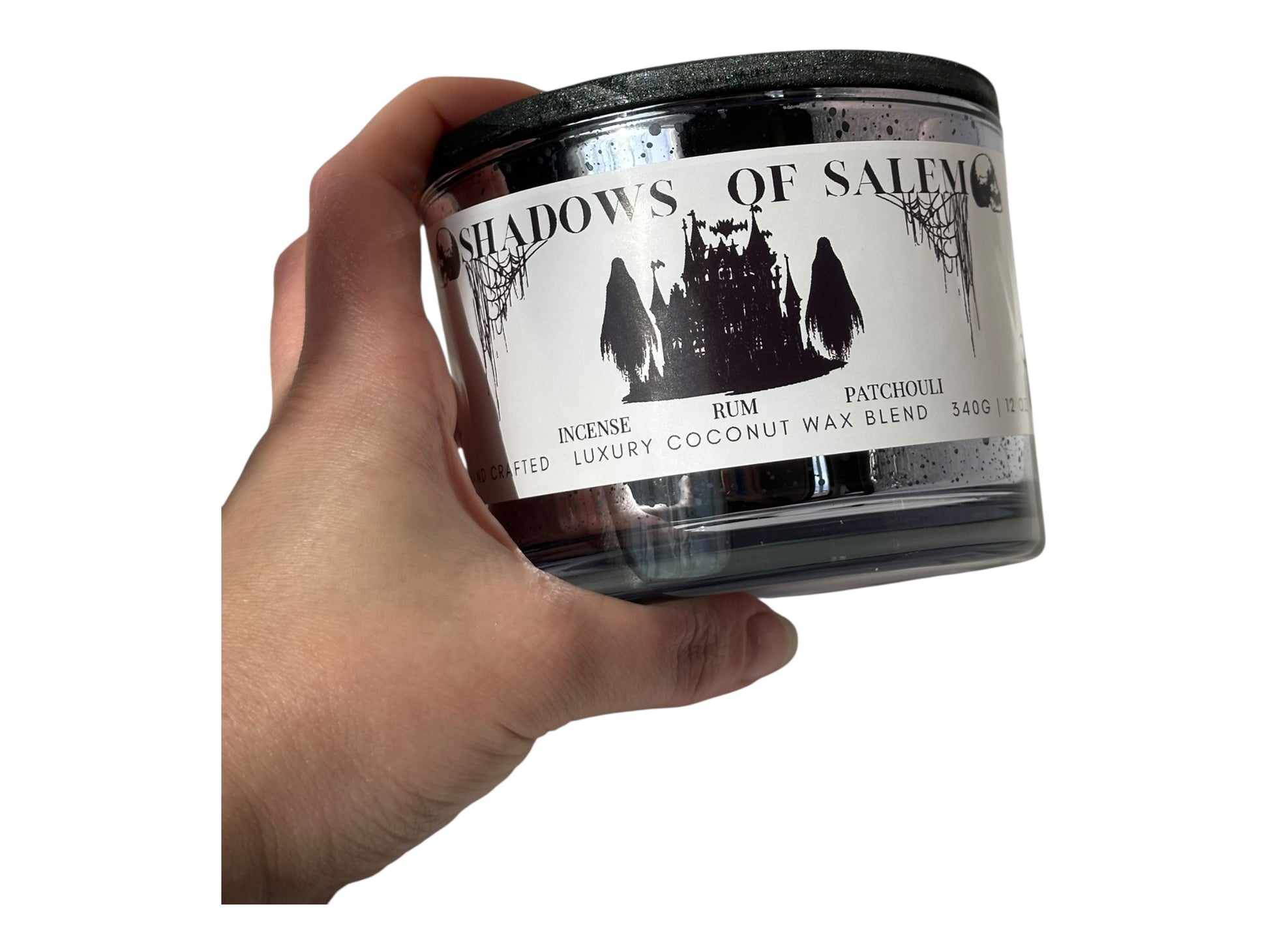 A hand holding a purple candle container labeled 'Shadows of Salem' with a white background.