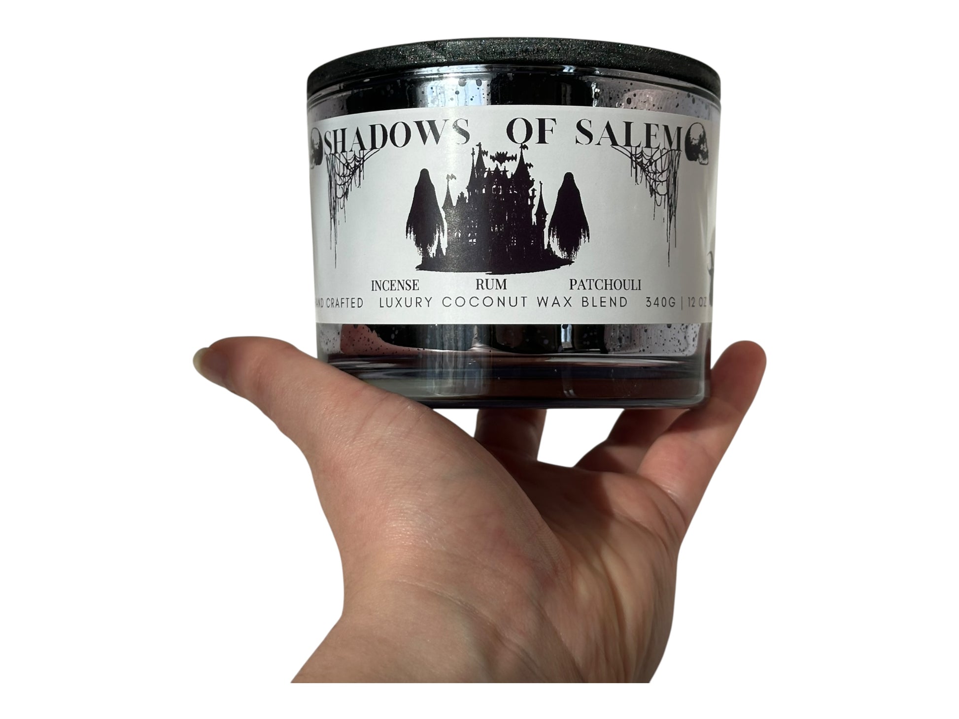 A purple candle jar labeled 'Shadows of Salem' held in a hand against a white background.