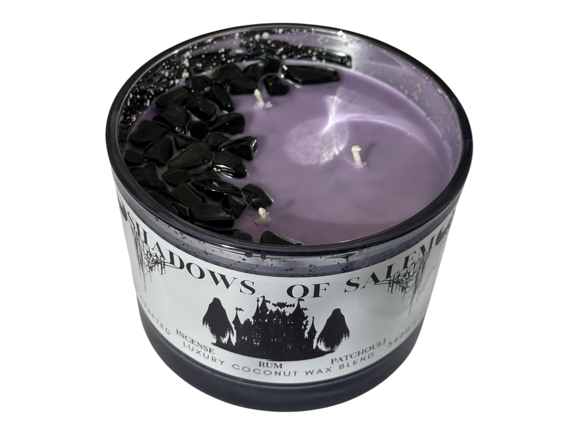 A purple candle with lid removed with three cotton wicks and obsidian gem stones in the shape of a crescent moon with a label "Shadows of Salem" on a white background.