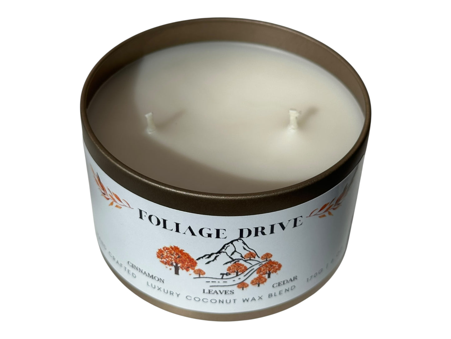 A gold candle tin with lid removed labeled 'Foliage Drive' on a white background.