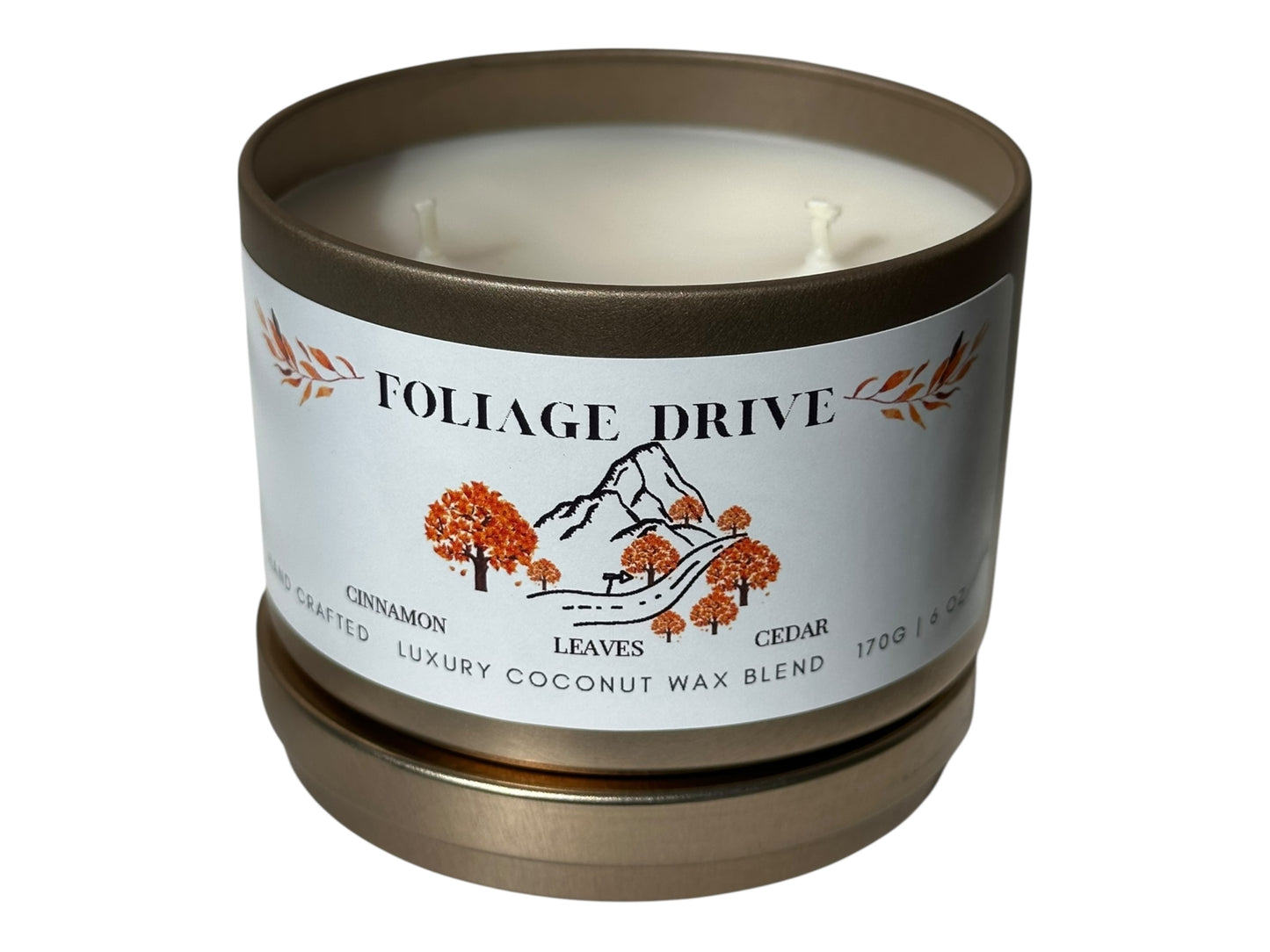 A gold candle tin with lid removed  showing two candle wicks and a smooth white candle top labeled 'Foliage Drive' label on a white background.