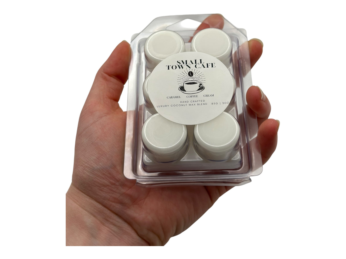 A hand holding a package of wax melts  labeled 'Small Town Cafe' on a white background.