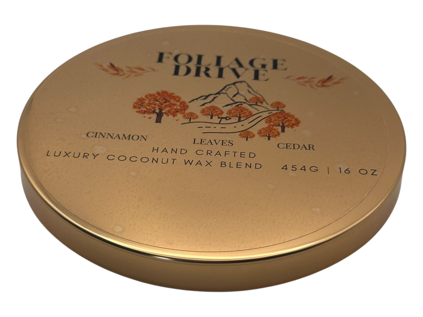 A  gold candle lid  labeled "Foliage Drive" with a decorative clear label lid on a white background.