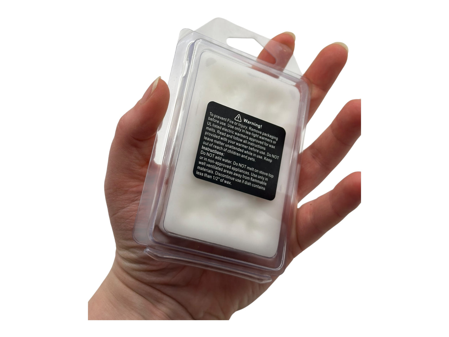 Hand holding a clear plastic clamshell with white wax melts and a black warning label on a white background
