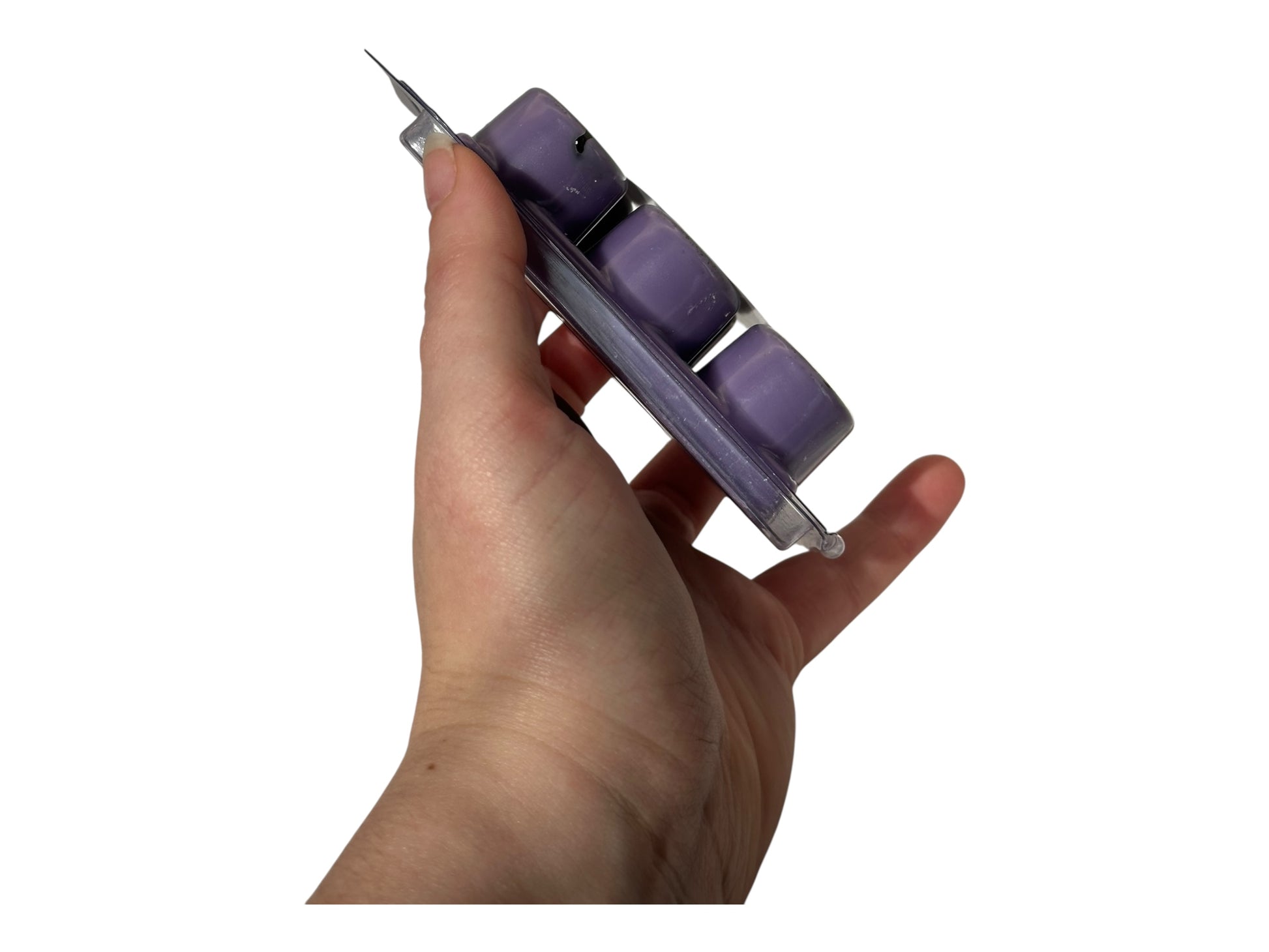A hand holding purple wax melts in a plastic clamshell on a white background. 
