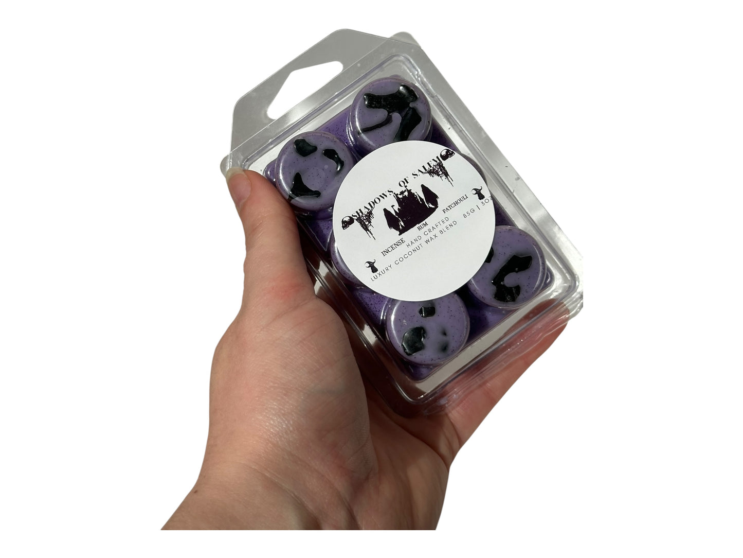 A hand holding purple wax melts labeled "Shadows of Salem" on a white background. 