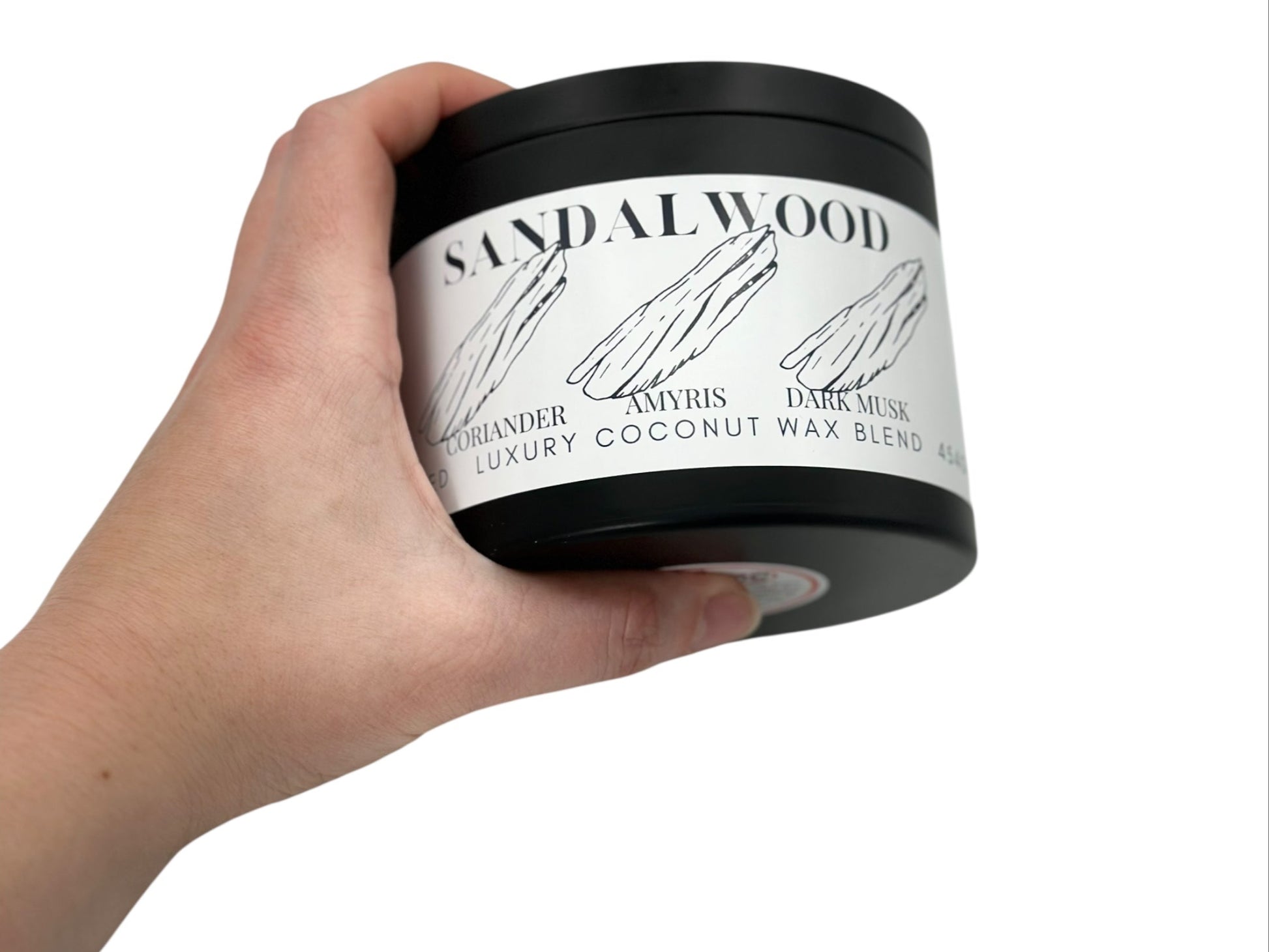 A hand holding a black candle tin labeled "Sandalwood" on a white background.