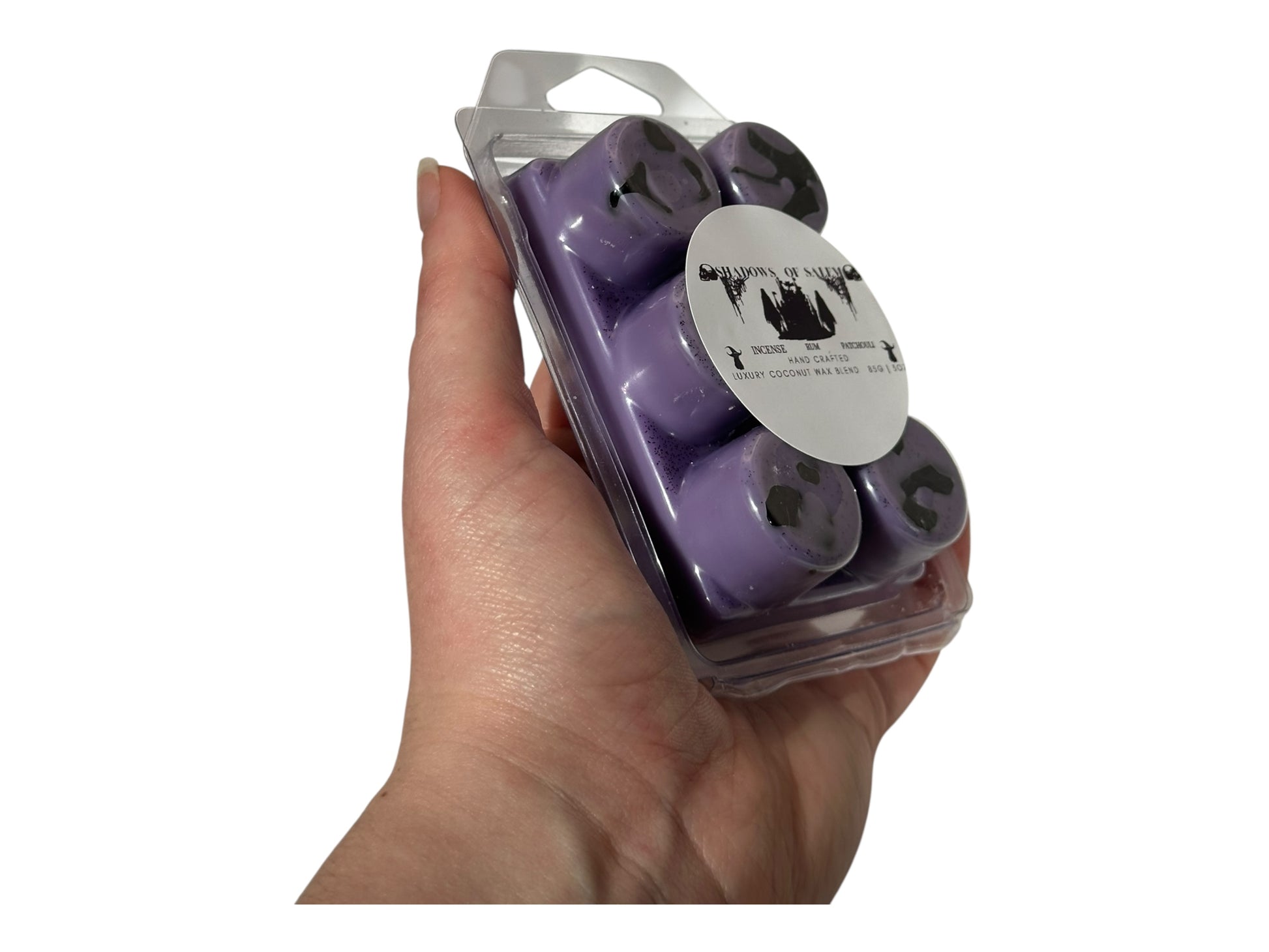 A hand holding a package of purple wax melts labeled "Shadows of Salem" on a white background. 