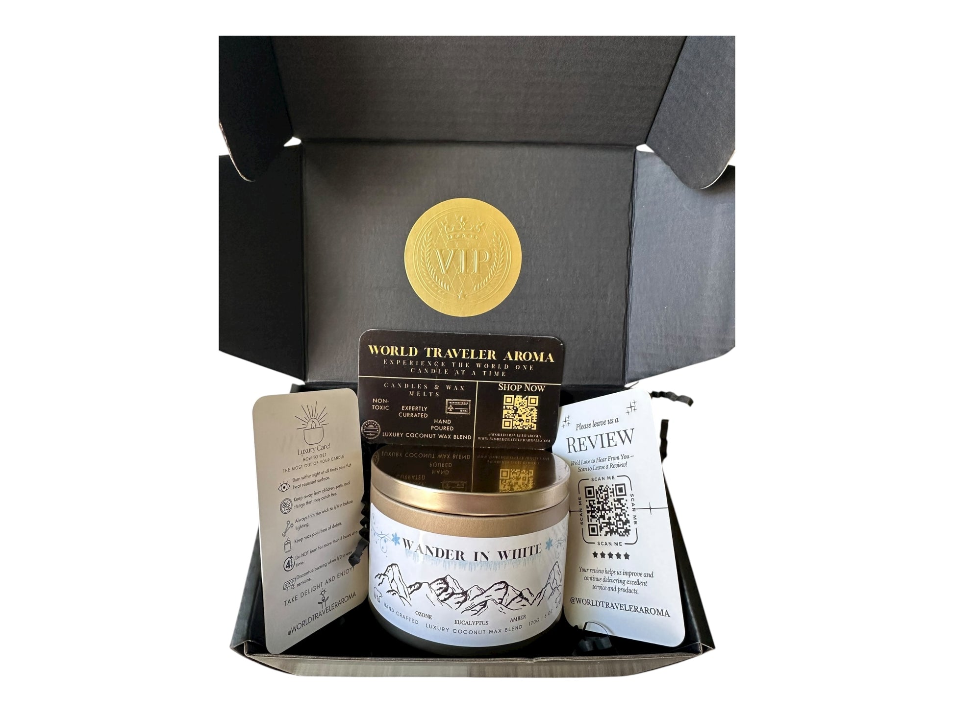 lack gift box with a gold VIP sticker on the lid inside the box a gold candle tin labeled "Wander in White" a candle care card instructions, a please review us card, and a World Traveler Aroma business card on a white background.