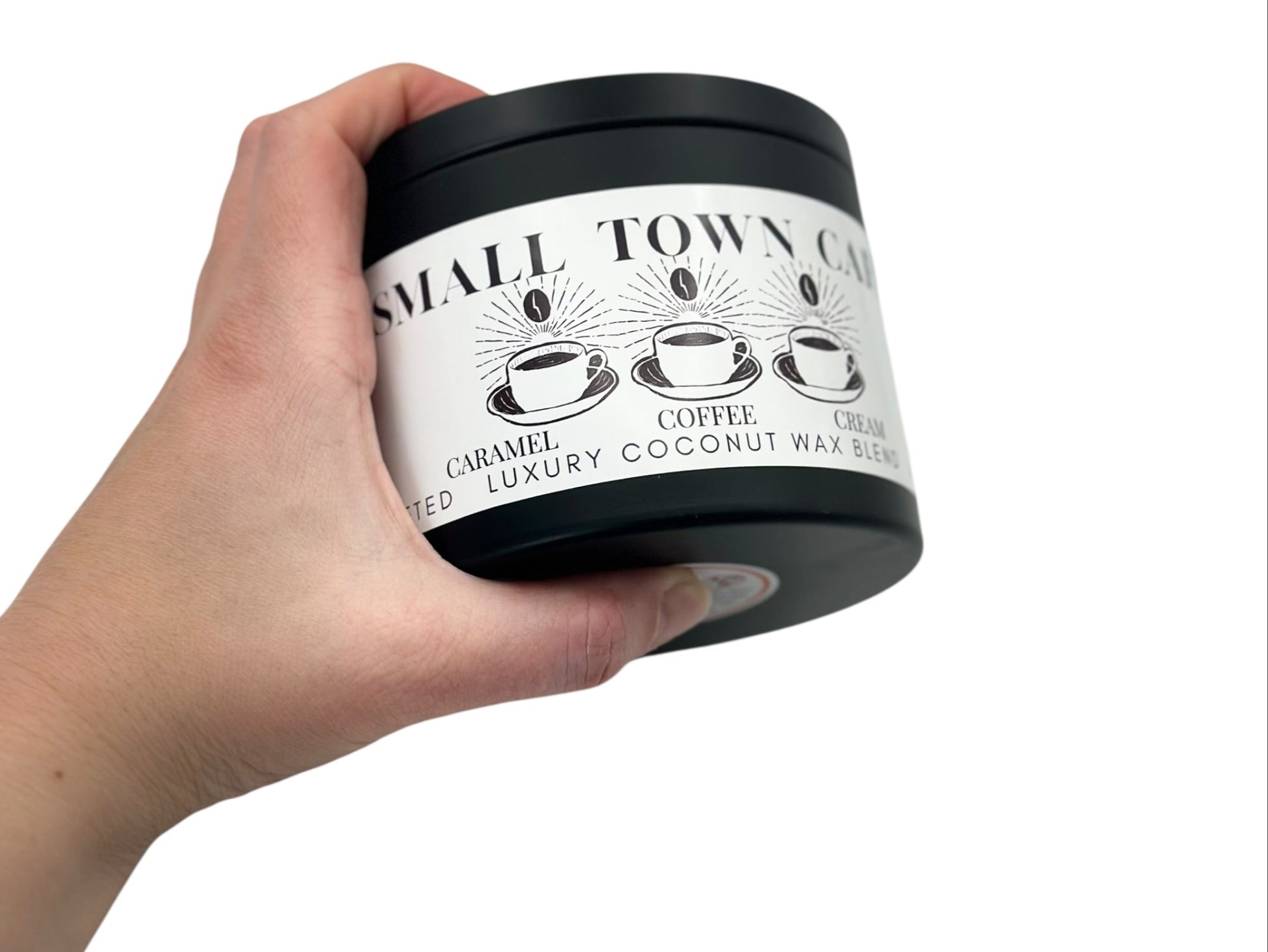 A hand holdingA black candle tin labeled "Small Town Cafe" on a white background.