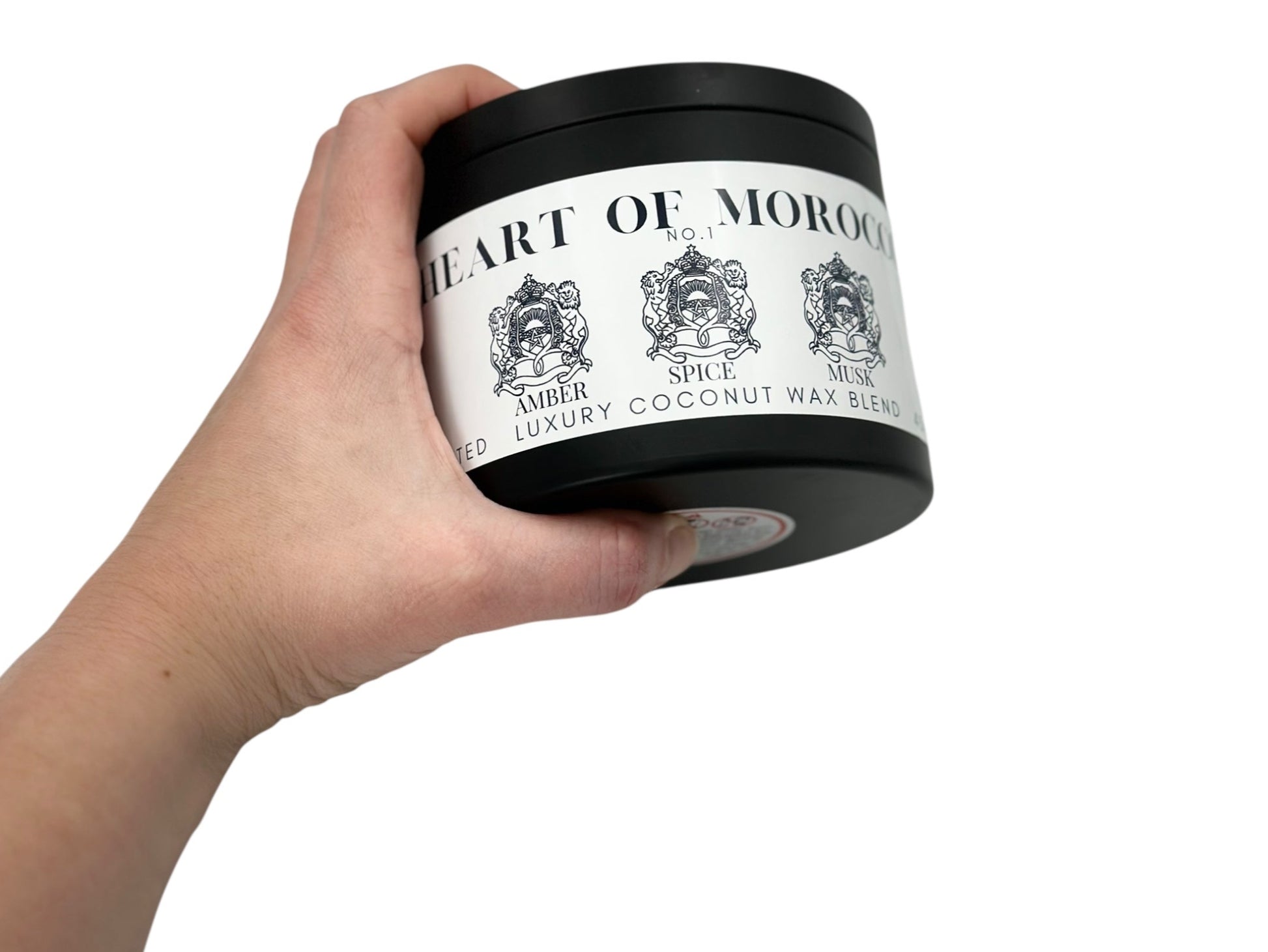 A hand holding a  black candle tin labeled "Heart of Morocco" on a white background.