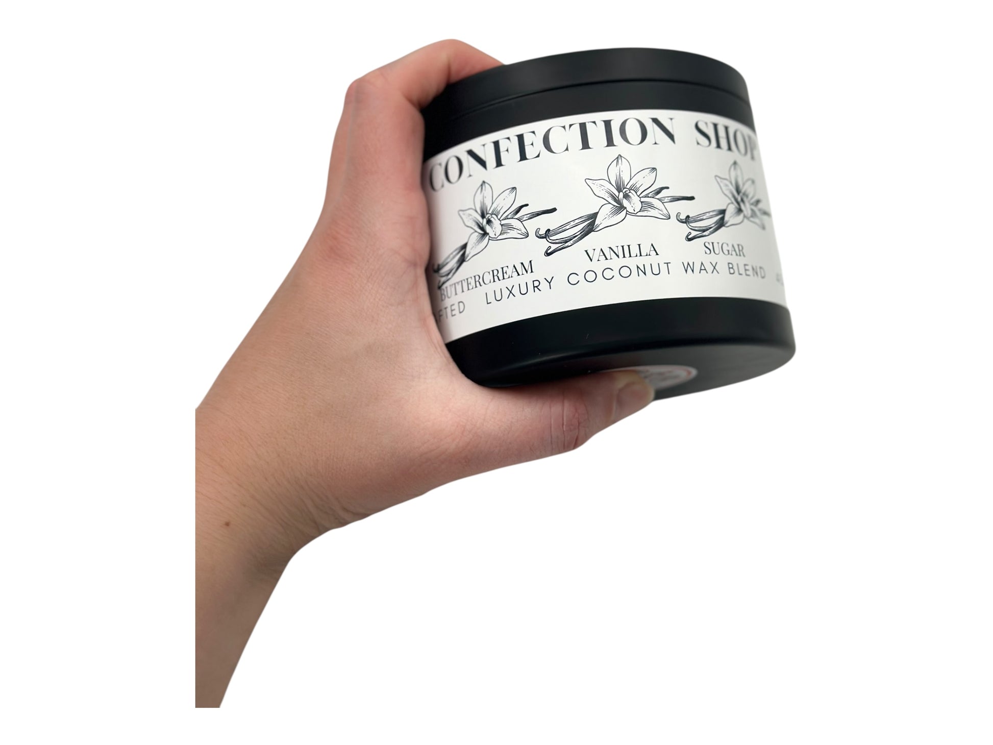 A hand holding a black candle tin labeled 'Confection Shop' on a white background.