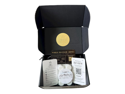 A black gift box with a gold VIP sticker on the lid with holiday wax melt labeled "Wander in White" a how to care card, please review card, and World Traveler Aroma Business Card on a white background.