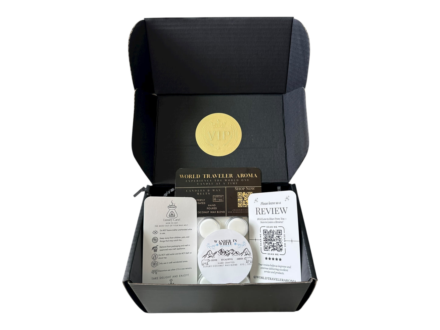 A black gift box with a gold VIP sticker on the lid with holiday wax melt labeled "Wander in White" a how to care card, please review card, and World Traveler Aroma Business Card on a white background.