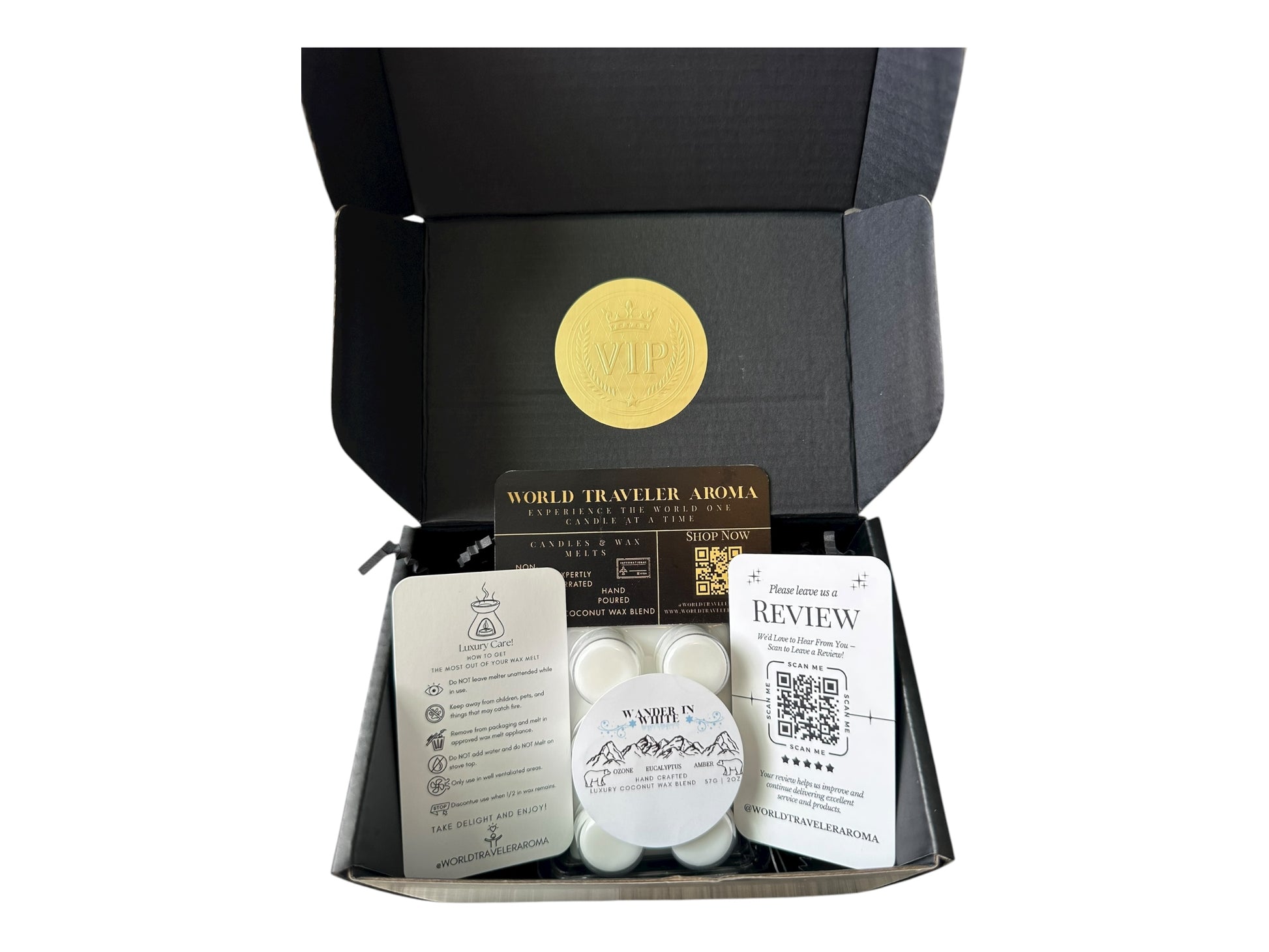A black gift box with a gold VIP sticker on the lid with holiday wax melt labeled "Wander in White" a how to care card, please review card, and World Traveler Aroma Business Card on a white background.