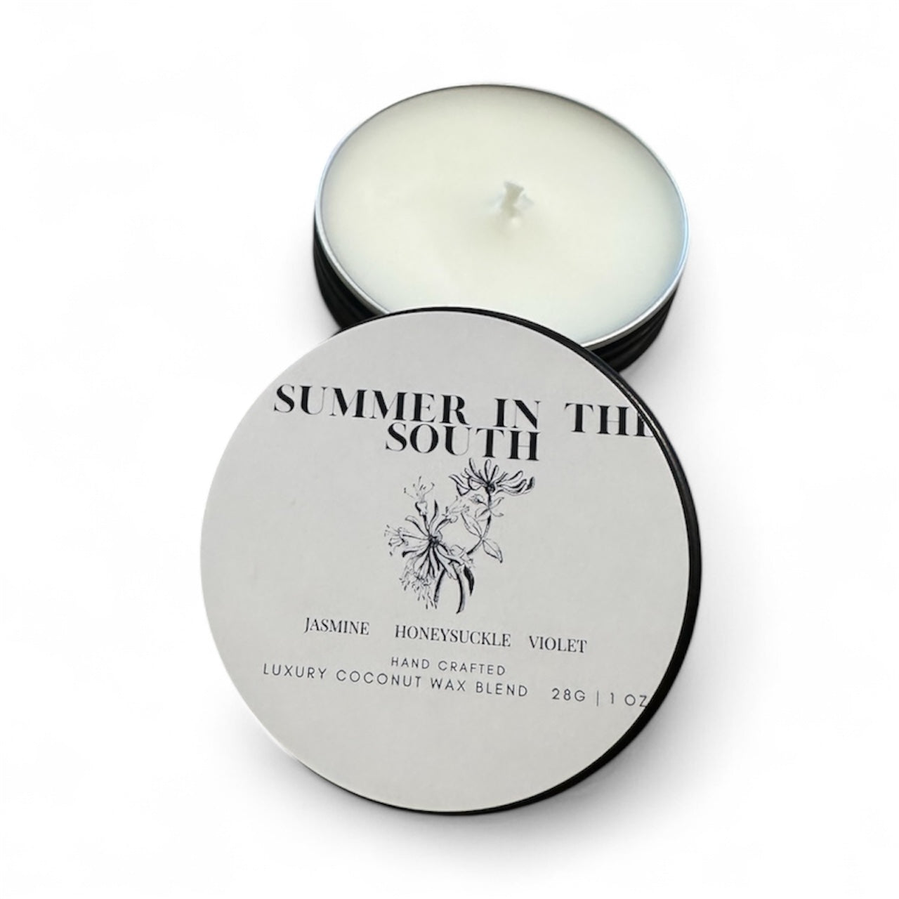 Travel sized 1oz candle tea light candle White wax with matte black tin and white label with black writing Honeysuckle, Jasmine, Violet Hand Crafted Luxury Coconut Wax Blend 28g 1oz  lid is removed and staged in the front table include impinge of honeysuckle flowering plant