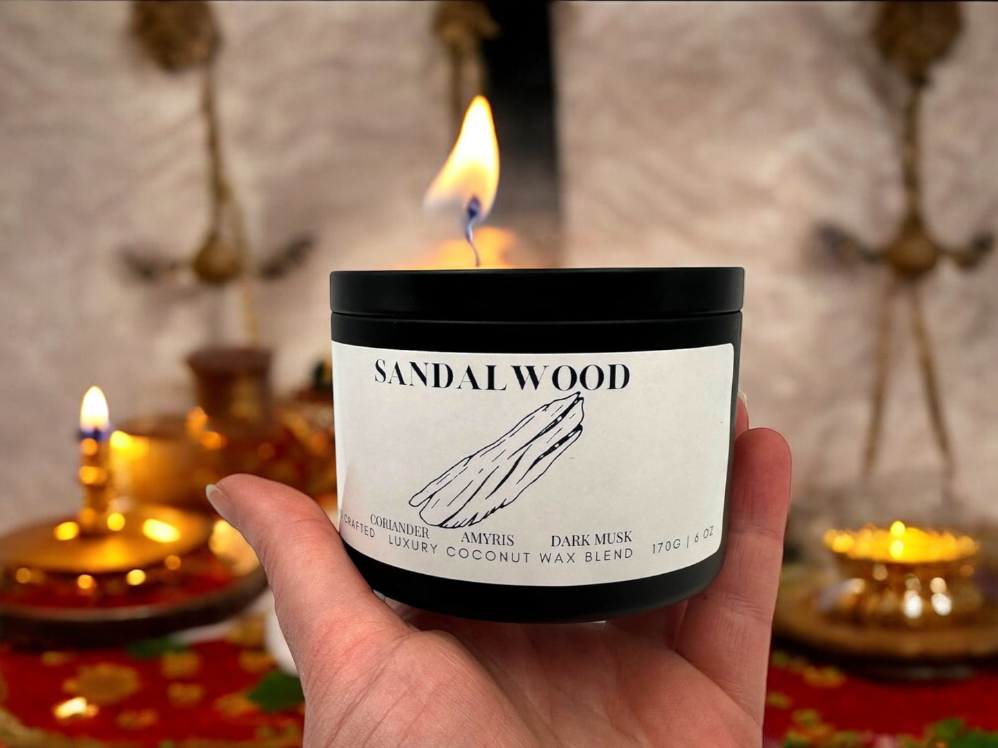 A black candle tin labeled "Sandalwood" with Diwali decorations in the background.
