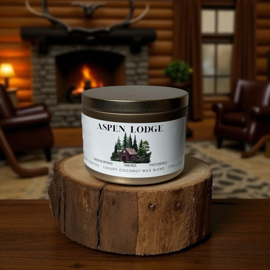 A gold candle tin  labeled 'Aspen Lodge' on a wooden stand with a fireplace a cabin living room in the background.