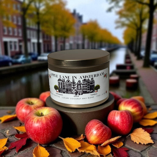 A gold candle tin  labeled 'Apple Lane in Amsterdam' with apples and autumn leaves on a autumn Amsterdam background.