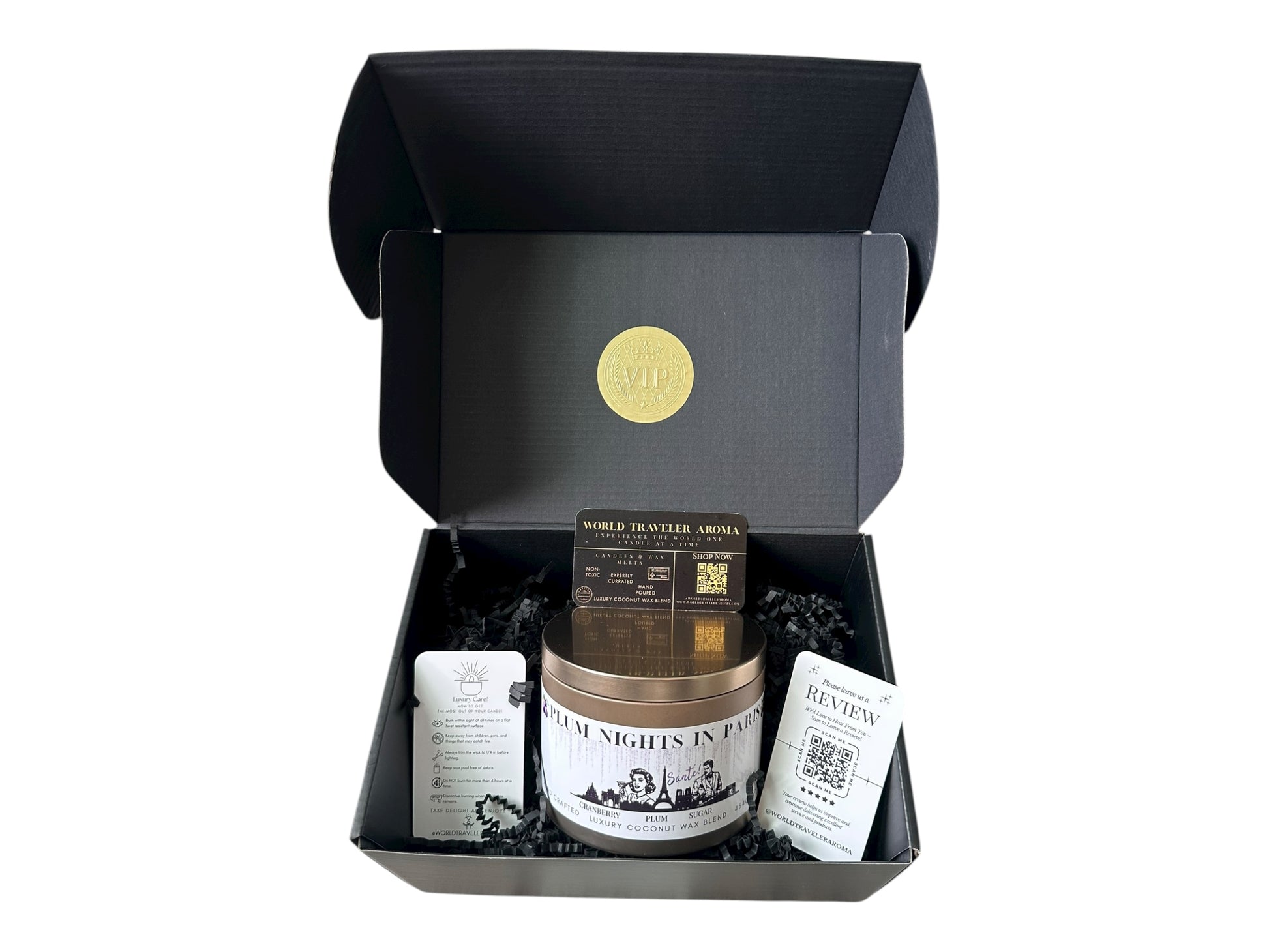 A black gift box with a gold VIP sticker on the lid inside the box a gold candle tin labeled "Plum Nights in Paris" a candle care care instructions, a please review us card, and a World Traveler Aroma business card on a white background.