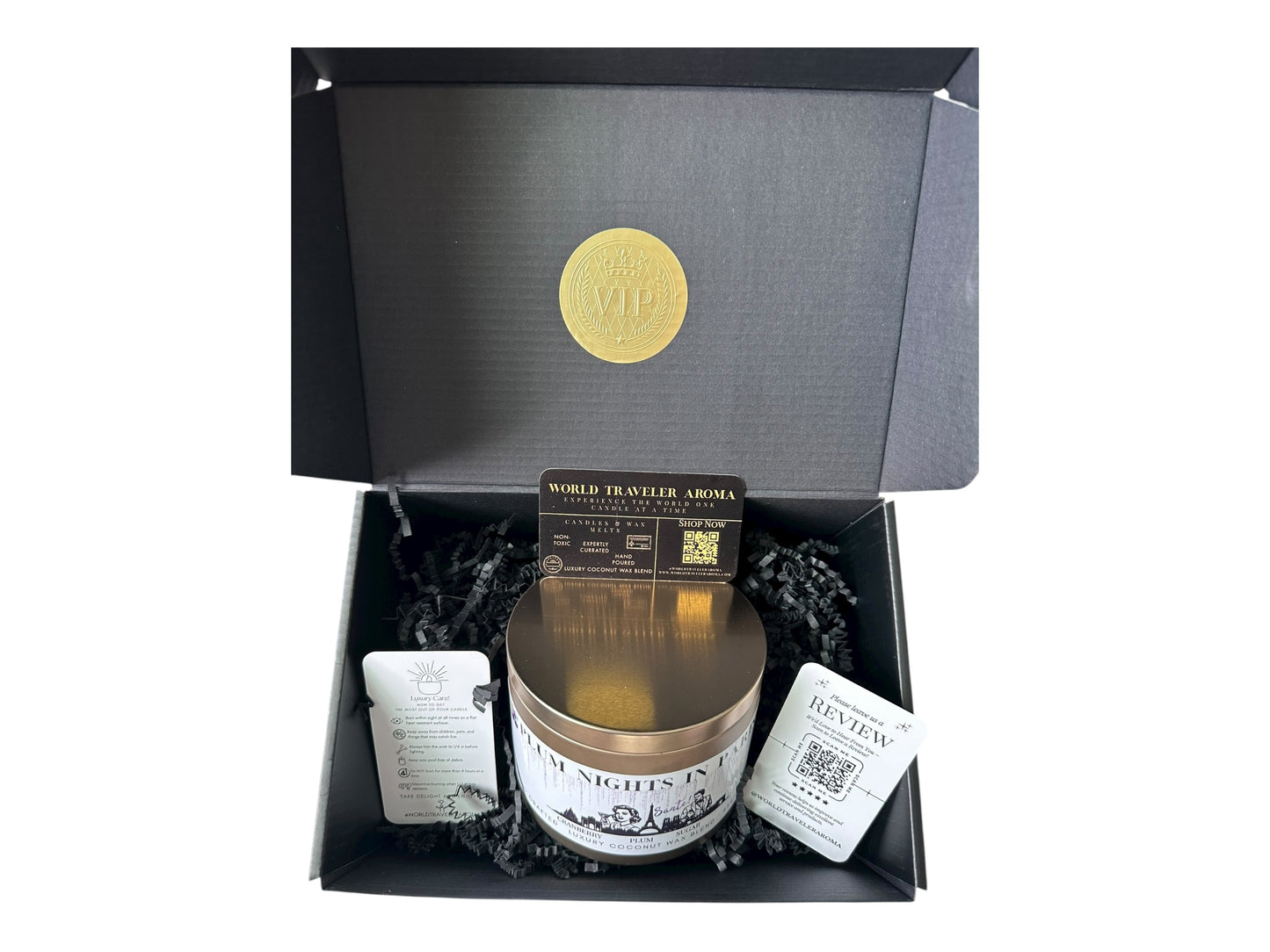 A black gift box with a gold VIP sticker on the lid inside the box a gold candle tin labeled "Plum Nights in Paris" a candle care care instructions, a please review us card, and a World Traveler Aroma business card on a white background.