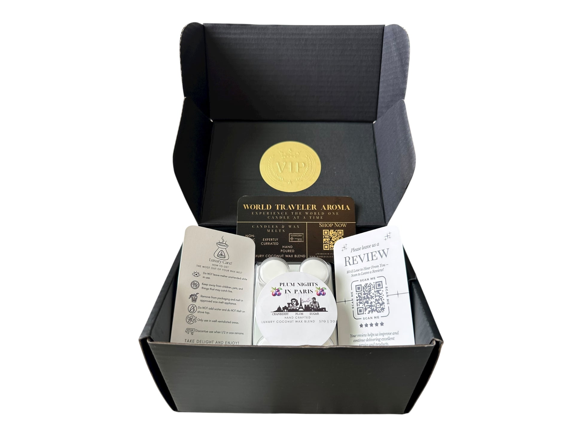 A black gift box with a golden VIP Sticker on the lid and inside the box a sugar plum scented wax melt labeled "Plum Nights in Pairs" a wax melt care instructions card, a please review us card, and World Traveler Aroma business card on a white background.