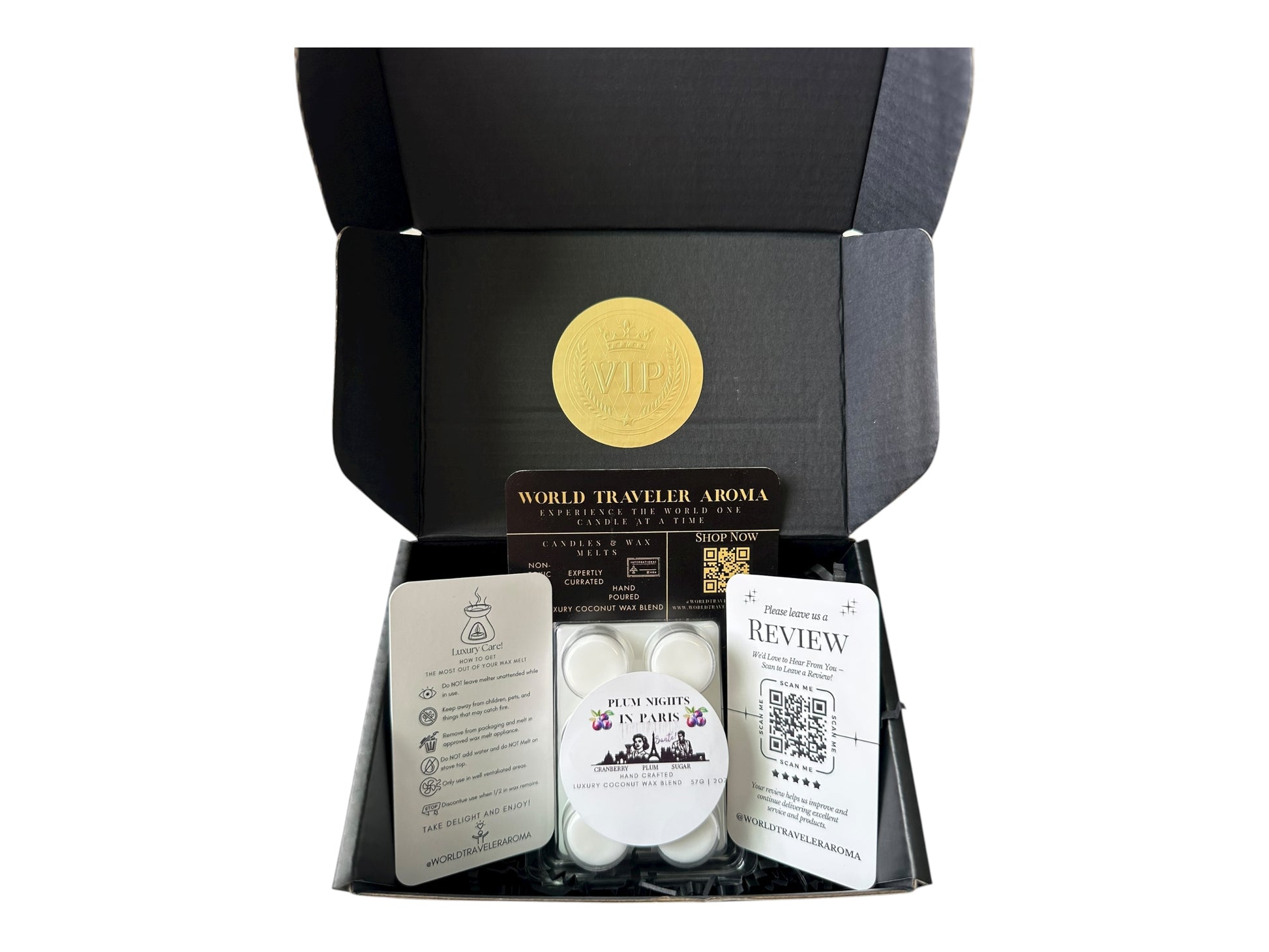 A black gift box with a golden VIP Sticker on the lid and inside the box a sugar plum scented wax melt labeled "Plum Nights in Pairs" a wax melt care instructions card, a please review us card, and World Traveler Aroma business card on a white background.