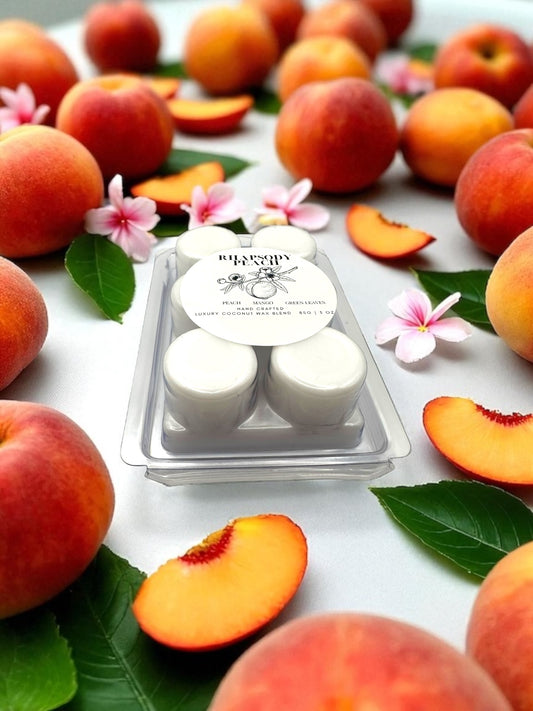 White wax melts in a clear container surrounded by peaches and flowers on a white background