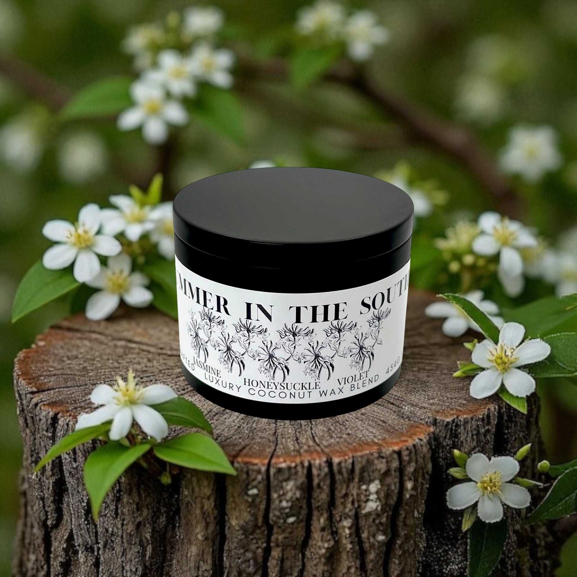 A black candle tin labeled Summer in the South resting on a wooden stump sourrounded by flowers. 