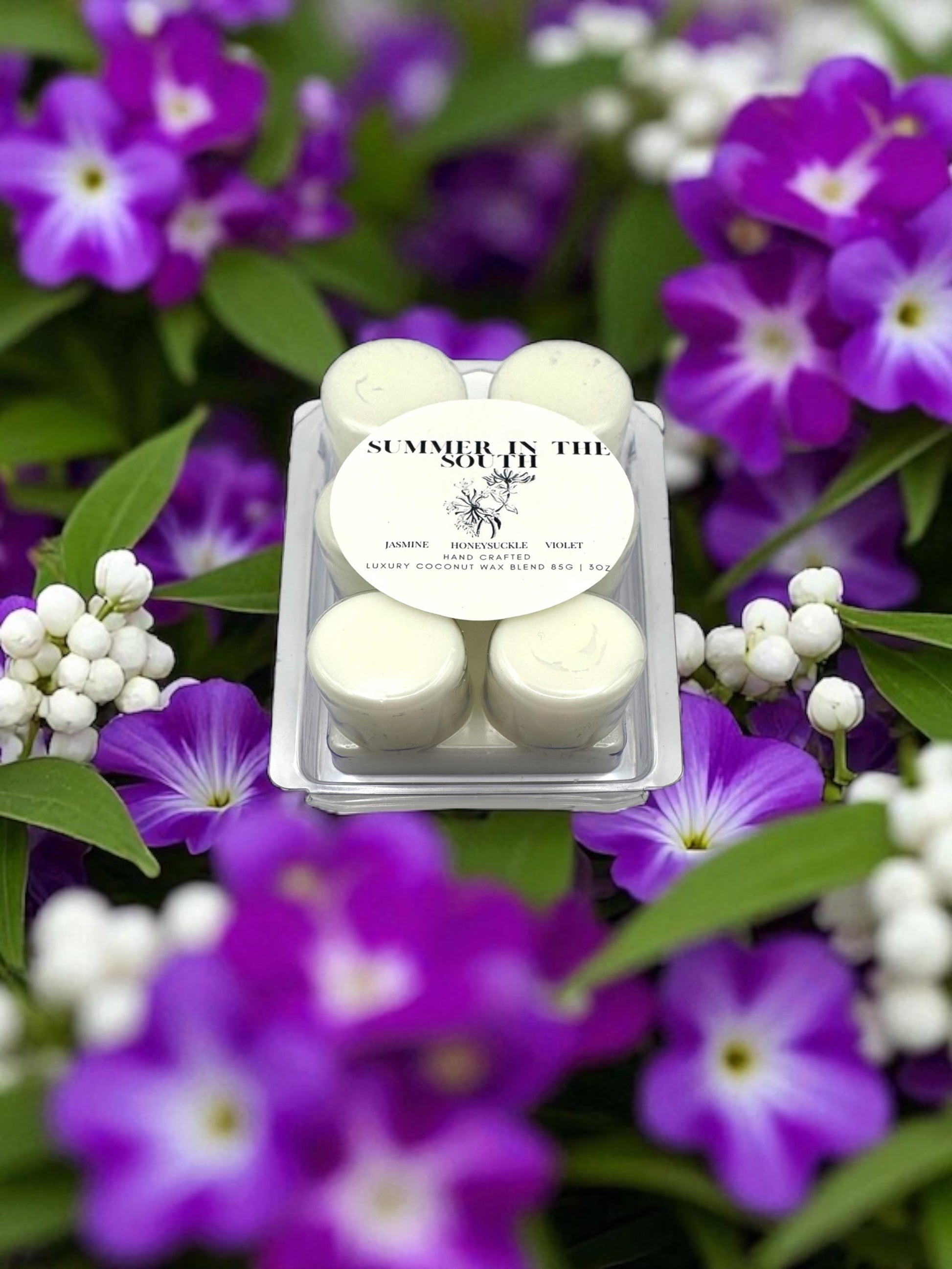 A wax melt in a clear clamshell labeled Summer in the South resting on a bed of flowers of violets and honeysuckle.