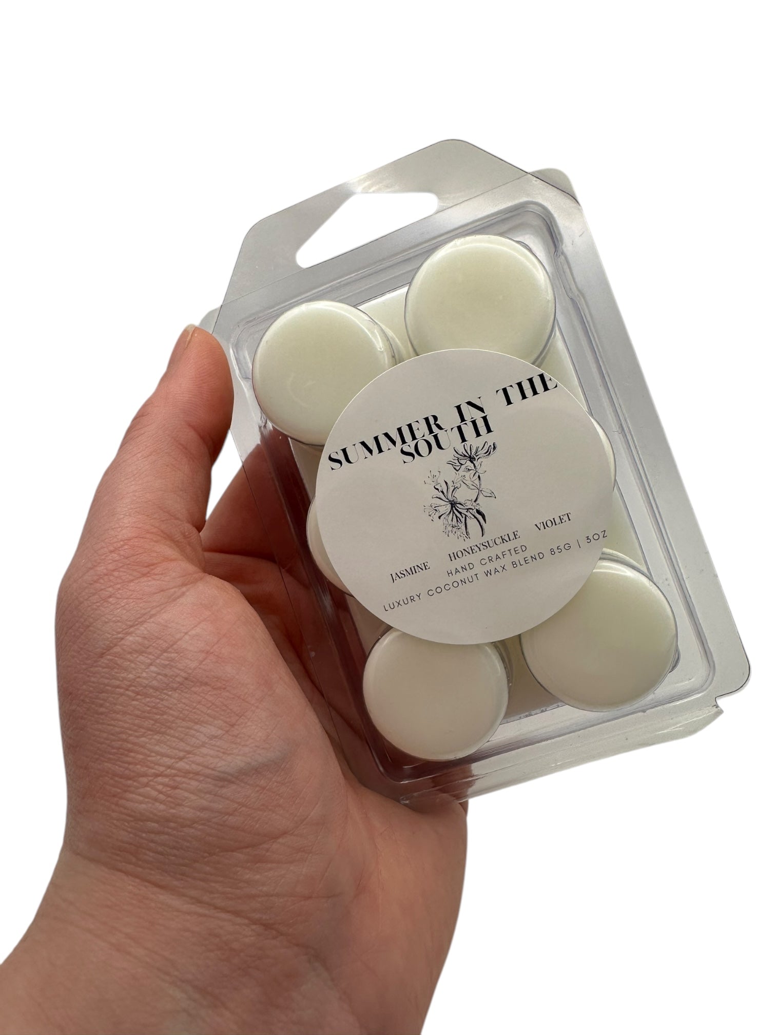 A hand holding a white wax melt labeled Summer in the South on a white background.