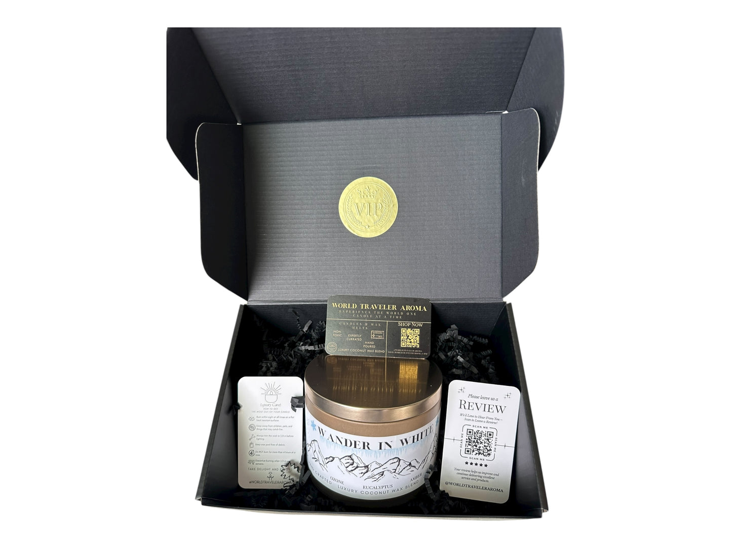 A black gift box with a gold VIP sticker on the lid inside the box a gold candle tin labeled "Wander in White", a candle care card instructions, a please review us card, and a World Traveler Aroma business card