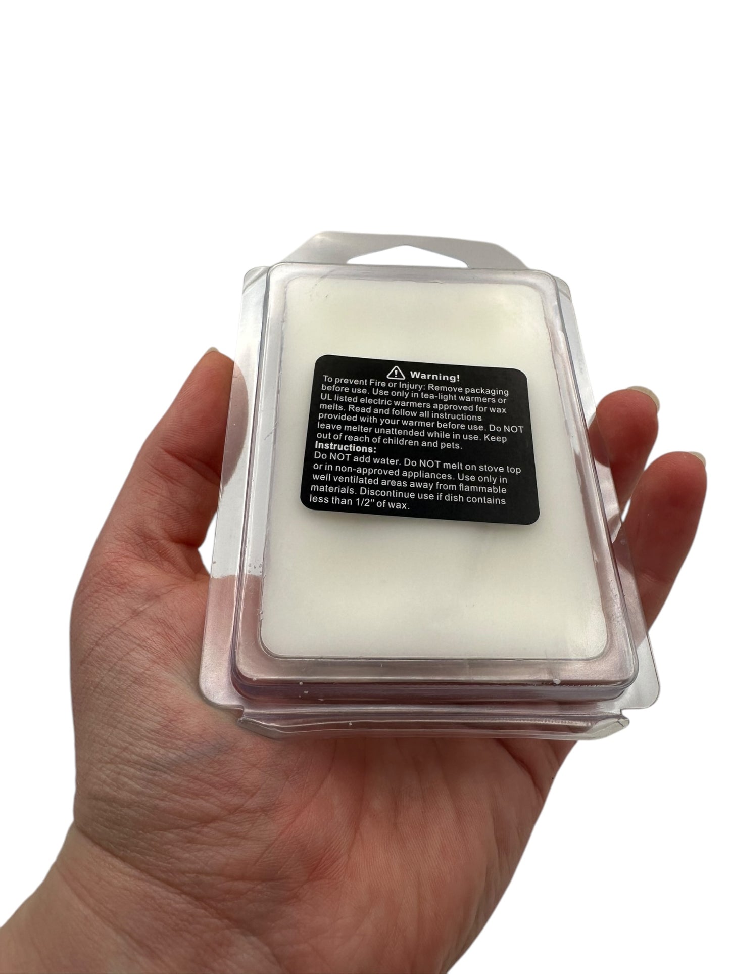 Hand holding a wax melt container with a warning label on a white background.