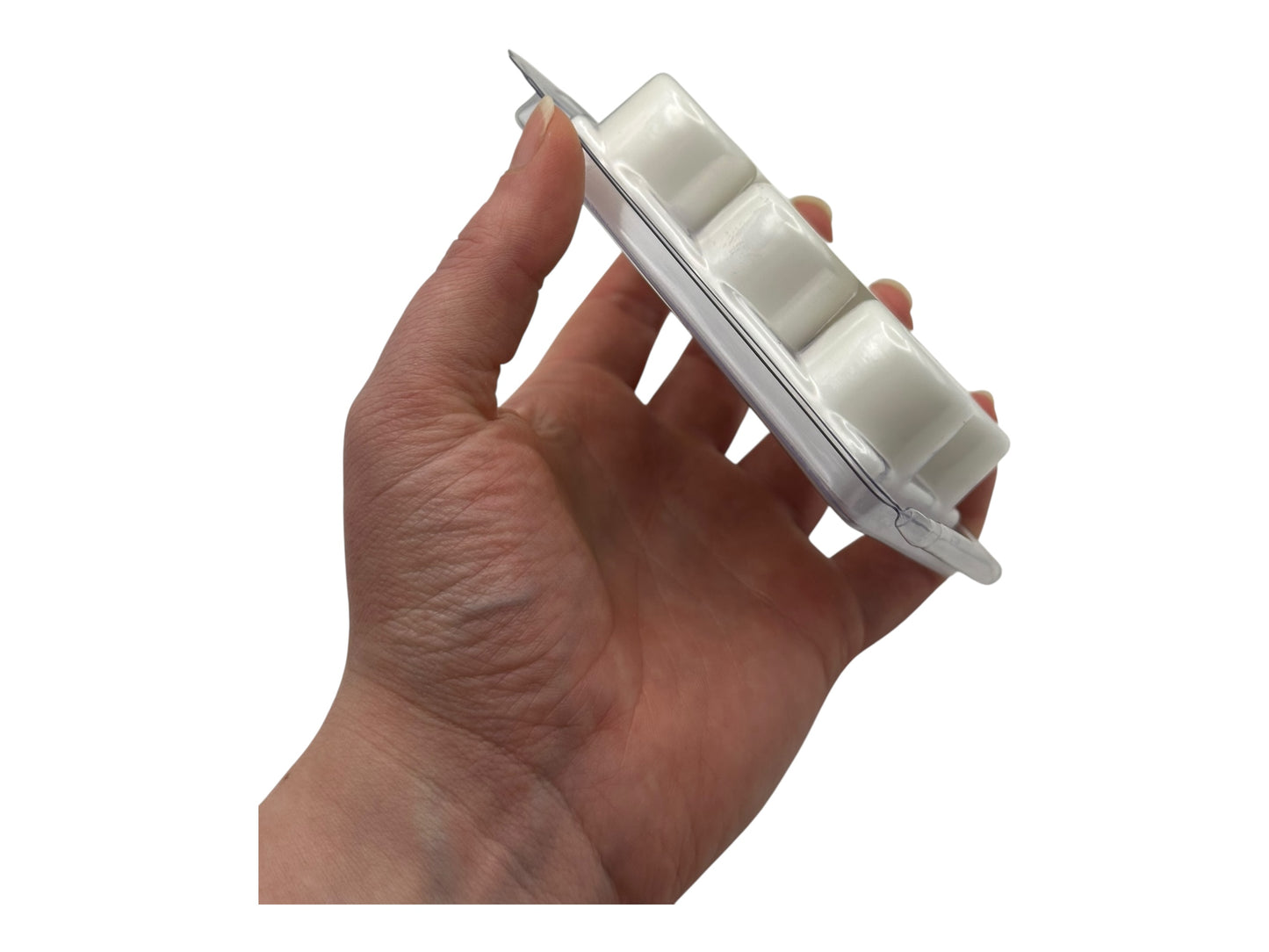 A hand holding a white wax melt in clear clamshell on a white background.