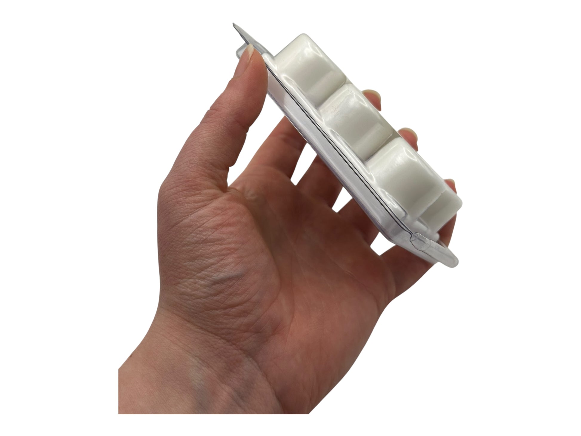 A hand holding a white wax melt in clear clamshell on a white background.